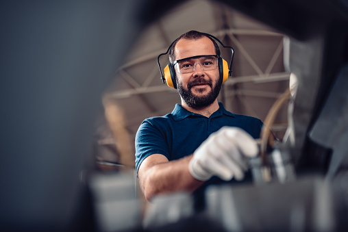 Factory worker operating band saw cutting machine for steel bars in the industrial factory