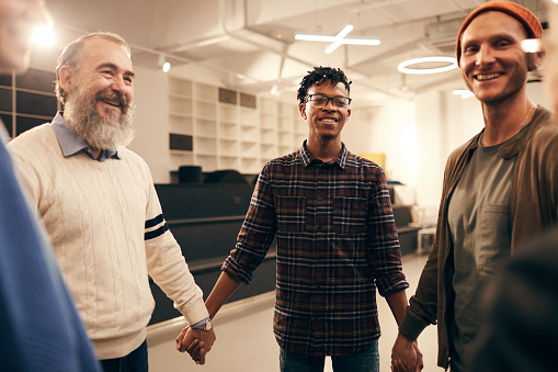 Group of happy people standing holding hands and smiling to each other during business training at office