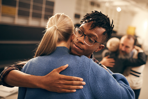 Young African man in eyeglasses embracing the young woman during therapy lesson