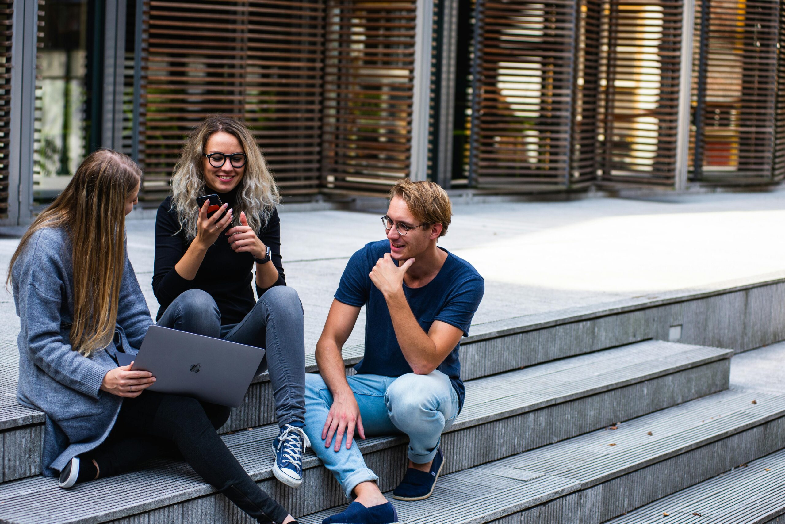 Three people talk with one another sitting on concrete stairs