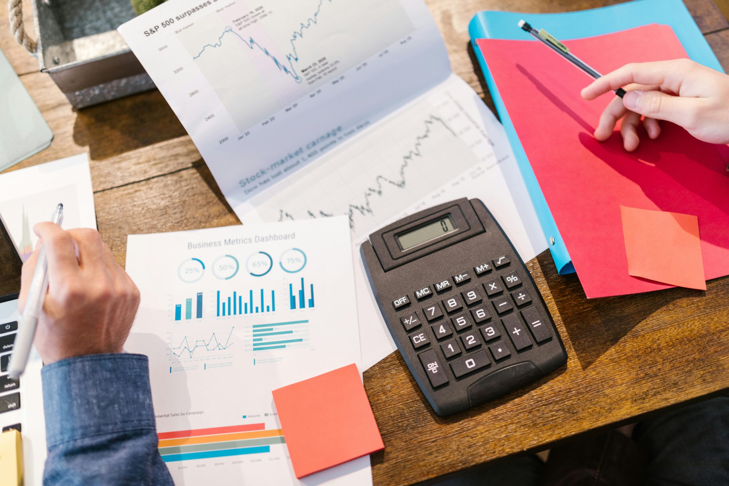 A desk messy with papers, a calulator, folders and pens