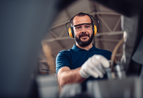A man wearing eye and ear protection works in a factory setting