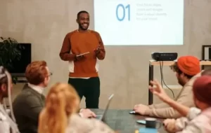 A man is presenting recovery resource materials in front of a group of four people sitting down. 