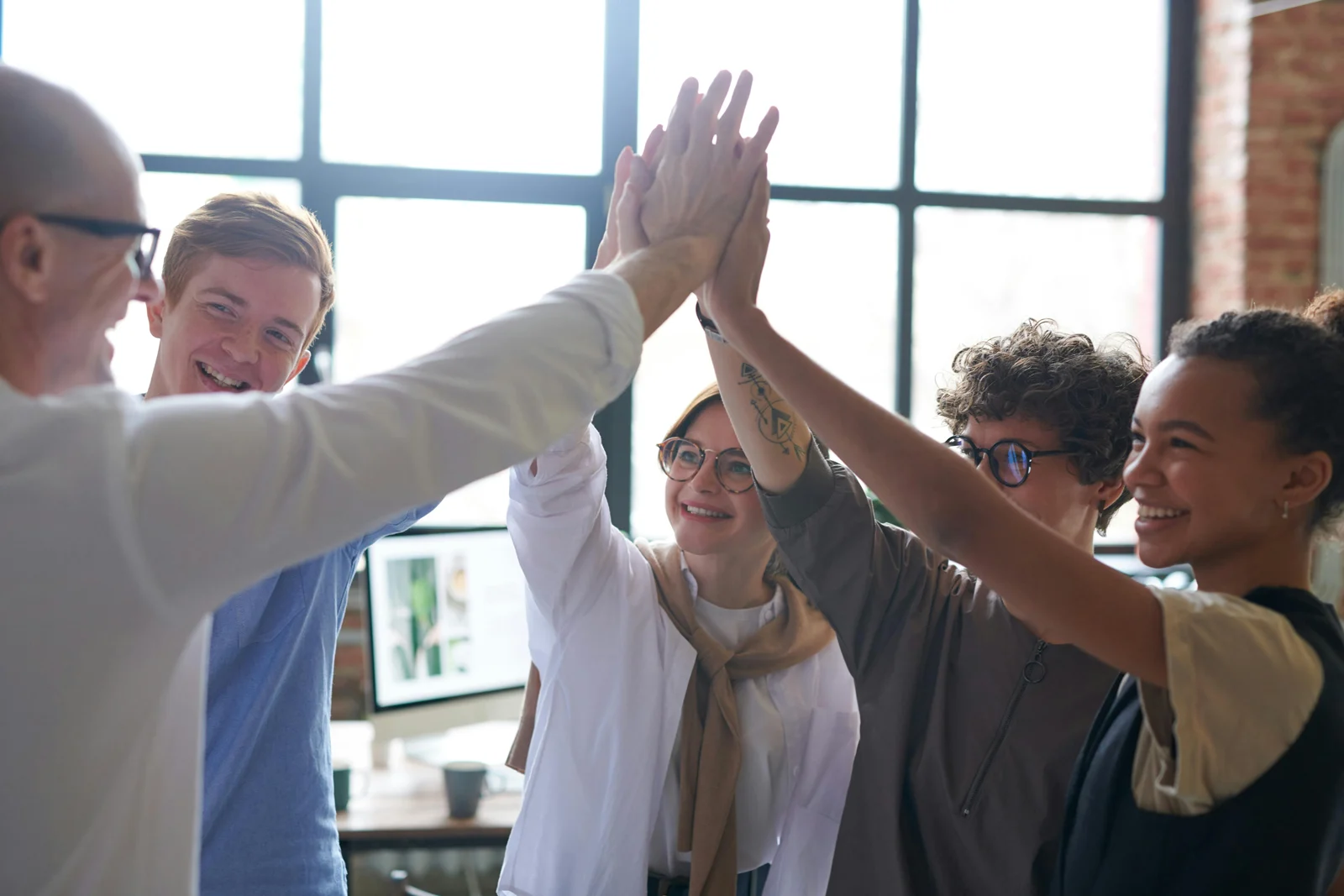 Five people standing next to a window all high five.