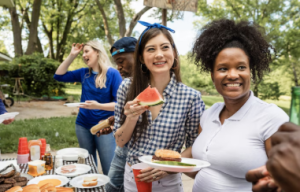 Four people in line are holding food items at a potluck.