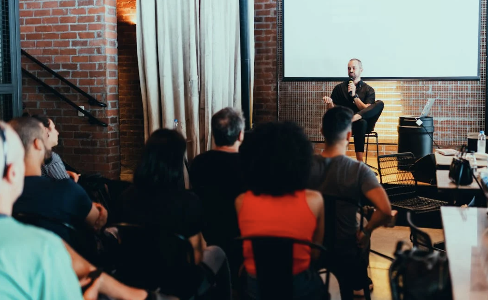 People sitting at a conference listening to a speaker holding a microphone.