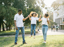 Two parents hold hands with their young daughter while walking in the grass