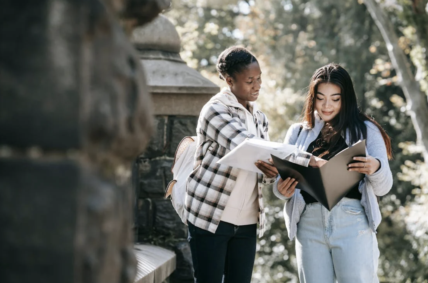 Two female students walking on campus while looking over notes.