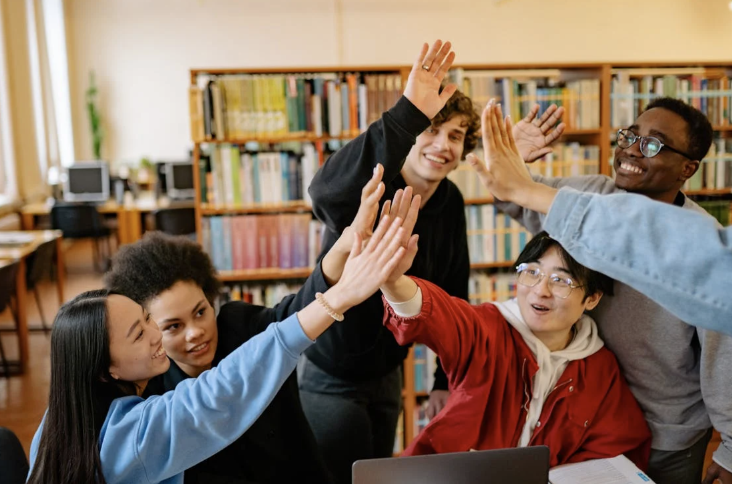 A group of students high-fiving in the library after finishing a group project.