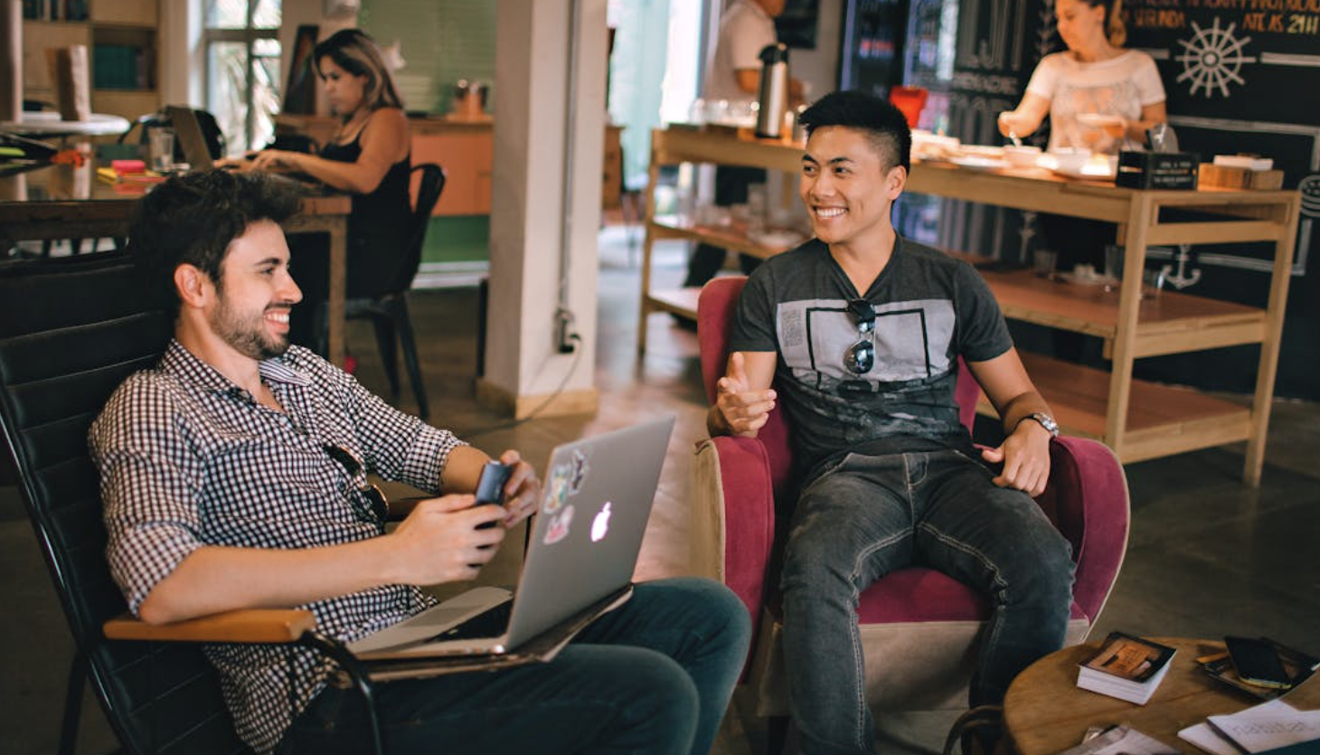 Two students talking to each other studying at a cafe.