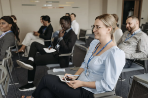 A woman in a blue shirt sits in the audience at a conference