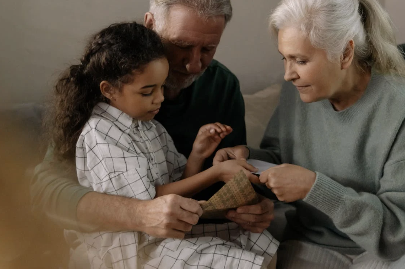 Grandparents helping their granddaughter open a present.