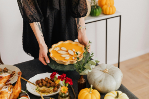 A person holding pumpkin pie over a table decorated with pumpkins
