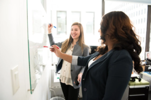 Women are smiling and writing on a whiteboard 