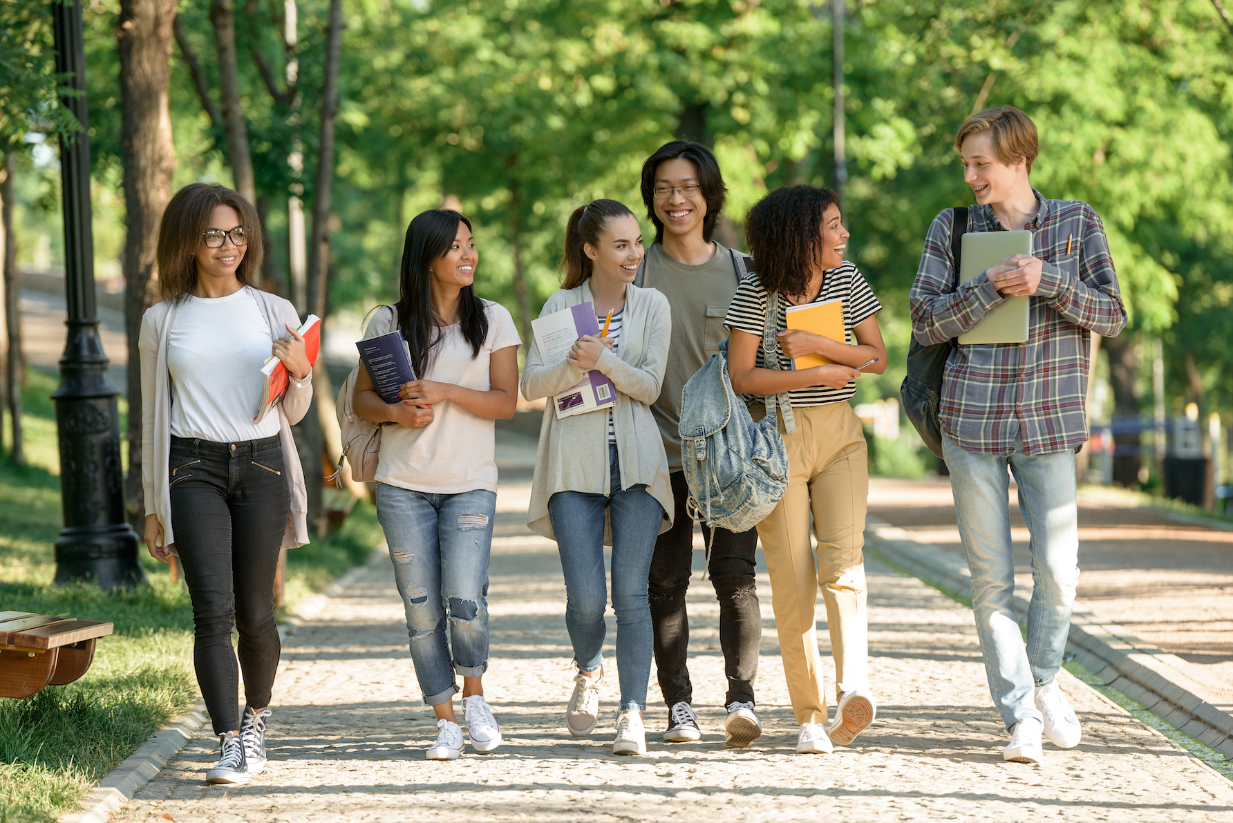 A group of six college students walks outdoors with trees behind them
