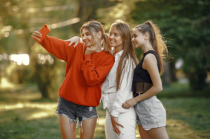 Three teenage girls stand outside and take a selfie