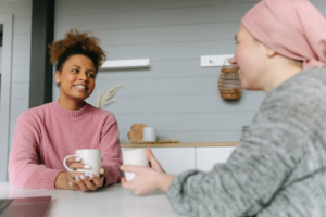 Two women sit at a table with coffee mugs and chat